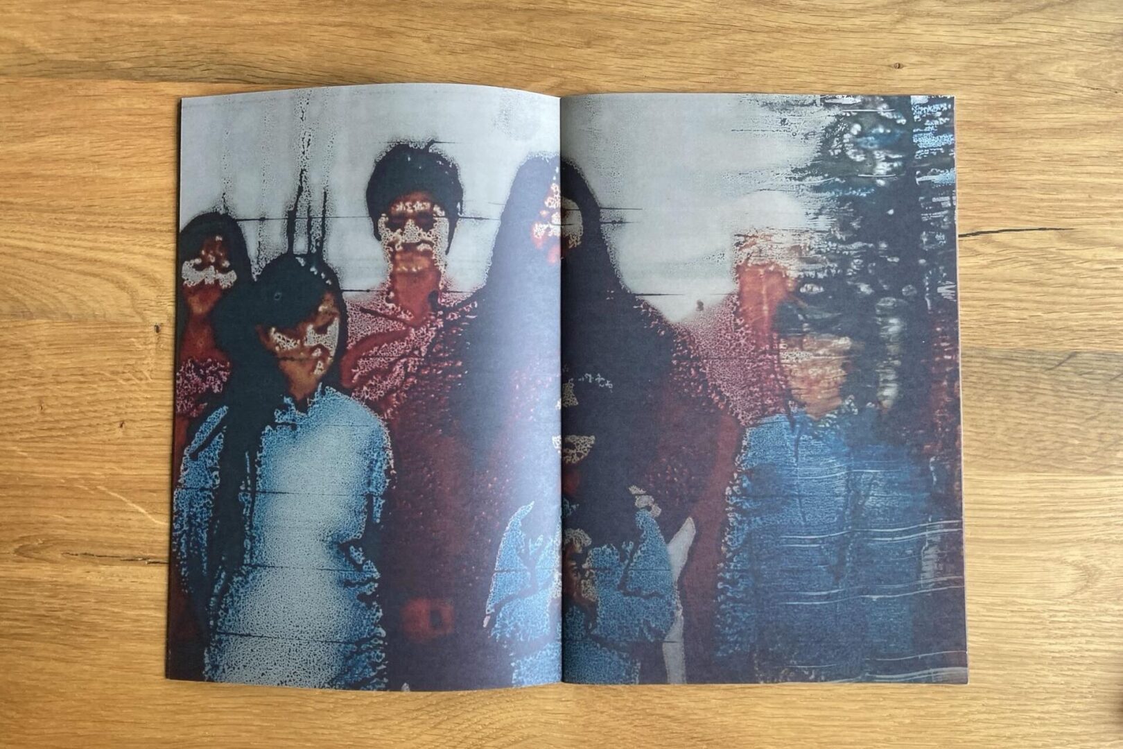 A magazine spread shows a distorted, low-resolution photo of a group of people standing together, with faces and features blurred and pixelated, on a wooden surface.