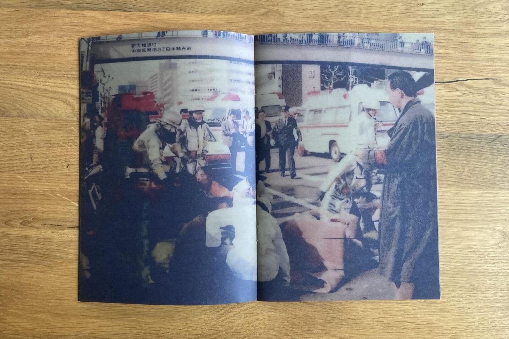 A printed photo in a book shows emergency responders assisting people lying on a street, with vehicles and bystanders nearby, under a highway overpass in an urban area.