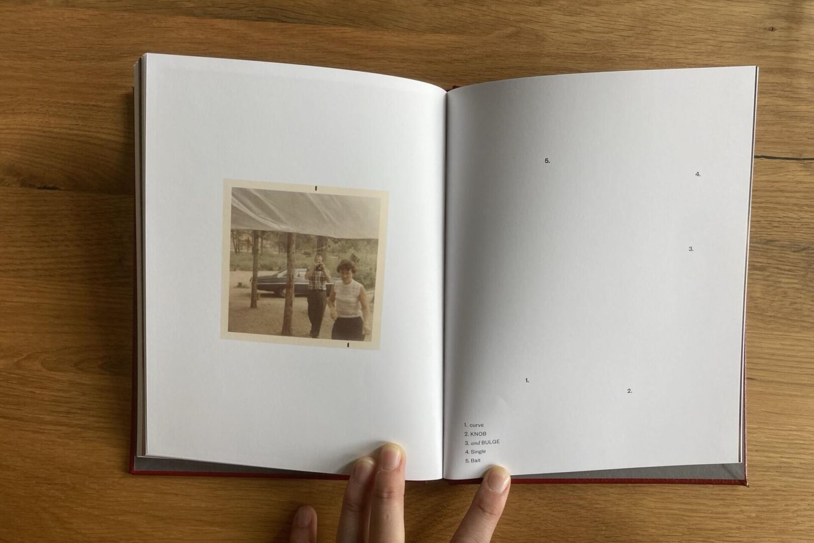 An open book on a wooden surface shows a vintage photo of two people standing outdoors on the left page and a list of five items with small numbered dots on the mostly blank right page.