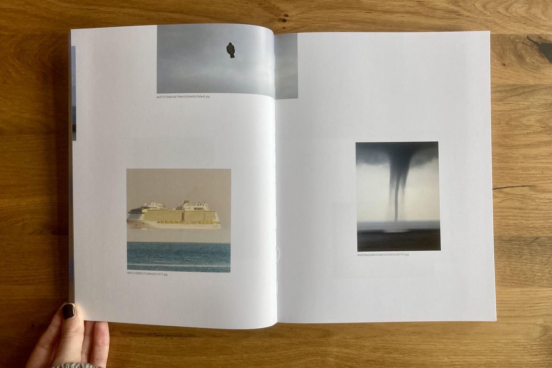 An open book rests on a wooden table. The left page shows a cruise ship at sea and a cloudy sky with a small balloon. The right page shows a waterspout touching down over the ocean under dark clouds. A hand holds the book’s left edge.