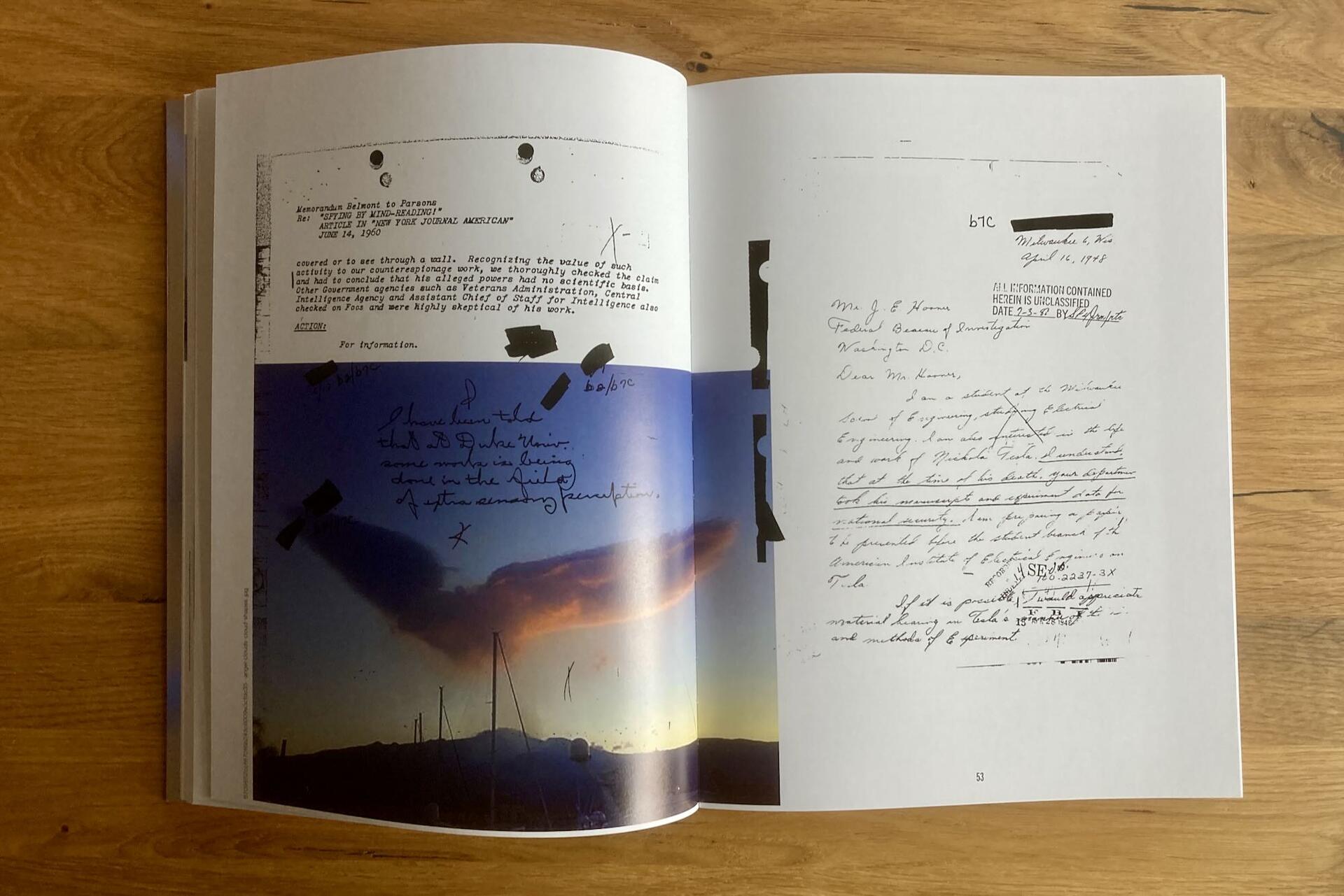An open book shows a page with a color photo of a cloud over a landscape, covered in handwritten notes and markings, next to a black-and-white scanned document with typewritten and handwritten text, both on a wooden surface.