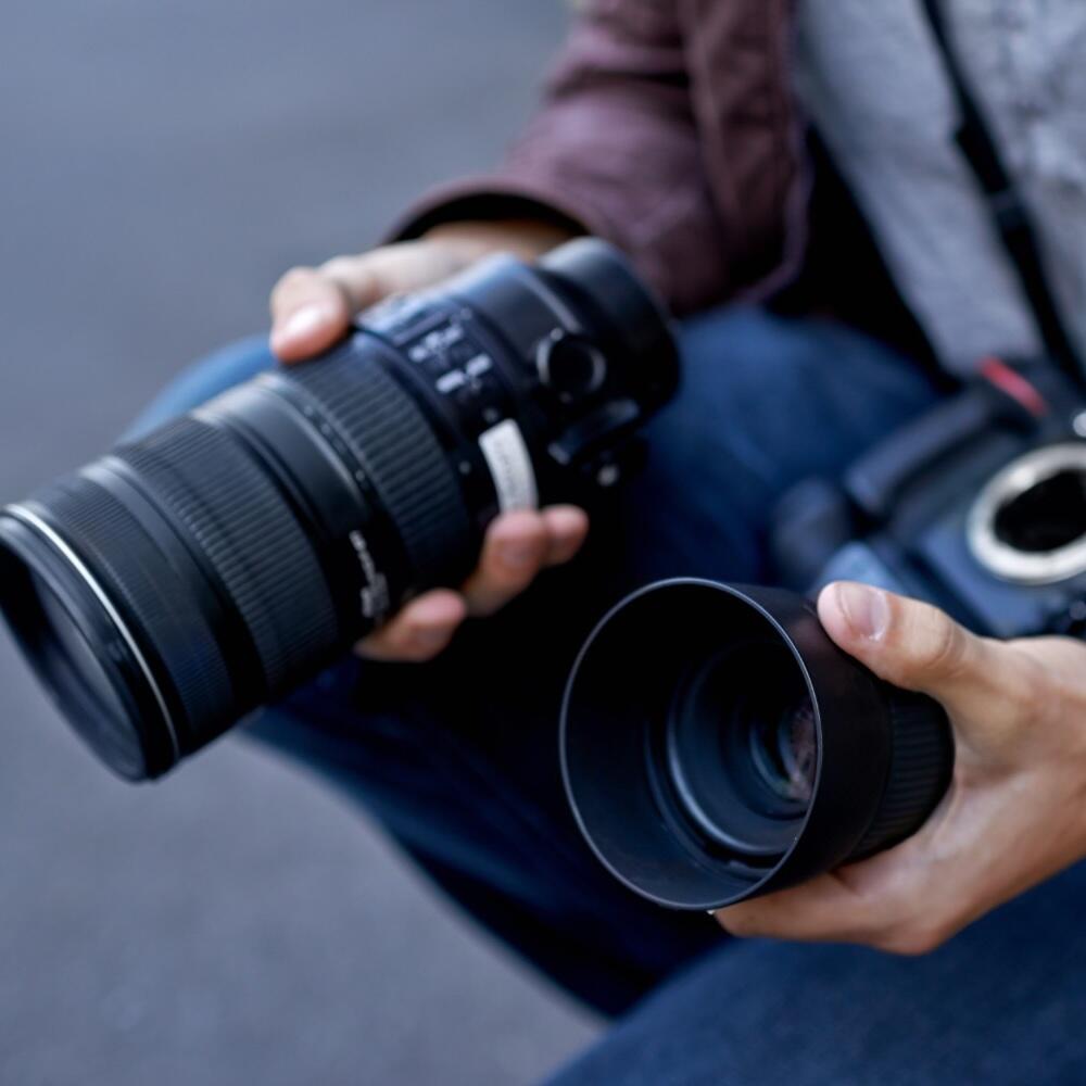 A person holding a DSLR camera with the lens detached in one hand and the camera body in the other, preparing to attach or remove the lens.