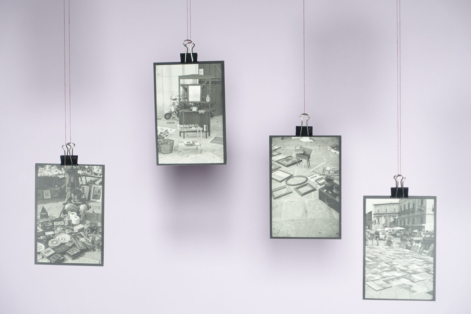 Four black-and-white photographs clipped to thin strings against a light background.