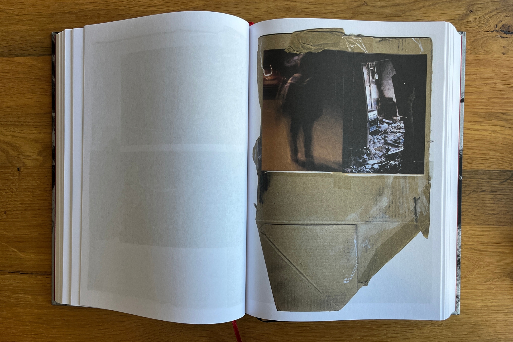 Open book on a wooden table showing a collage with brown tape, dark photographic fragments, and a muted colour image of a damaged interior.