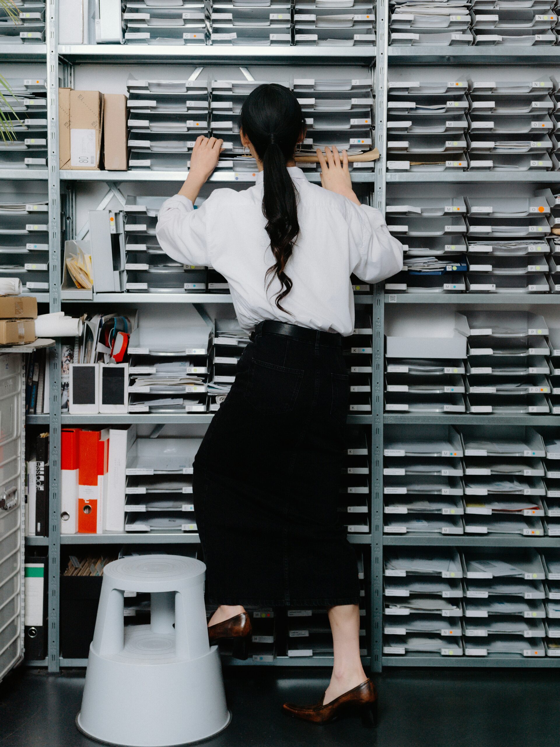 A feminine-presenting person organizes paperwork in labeled storage shelves.