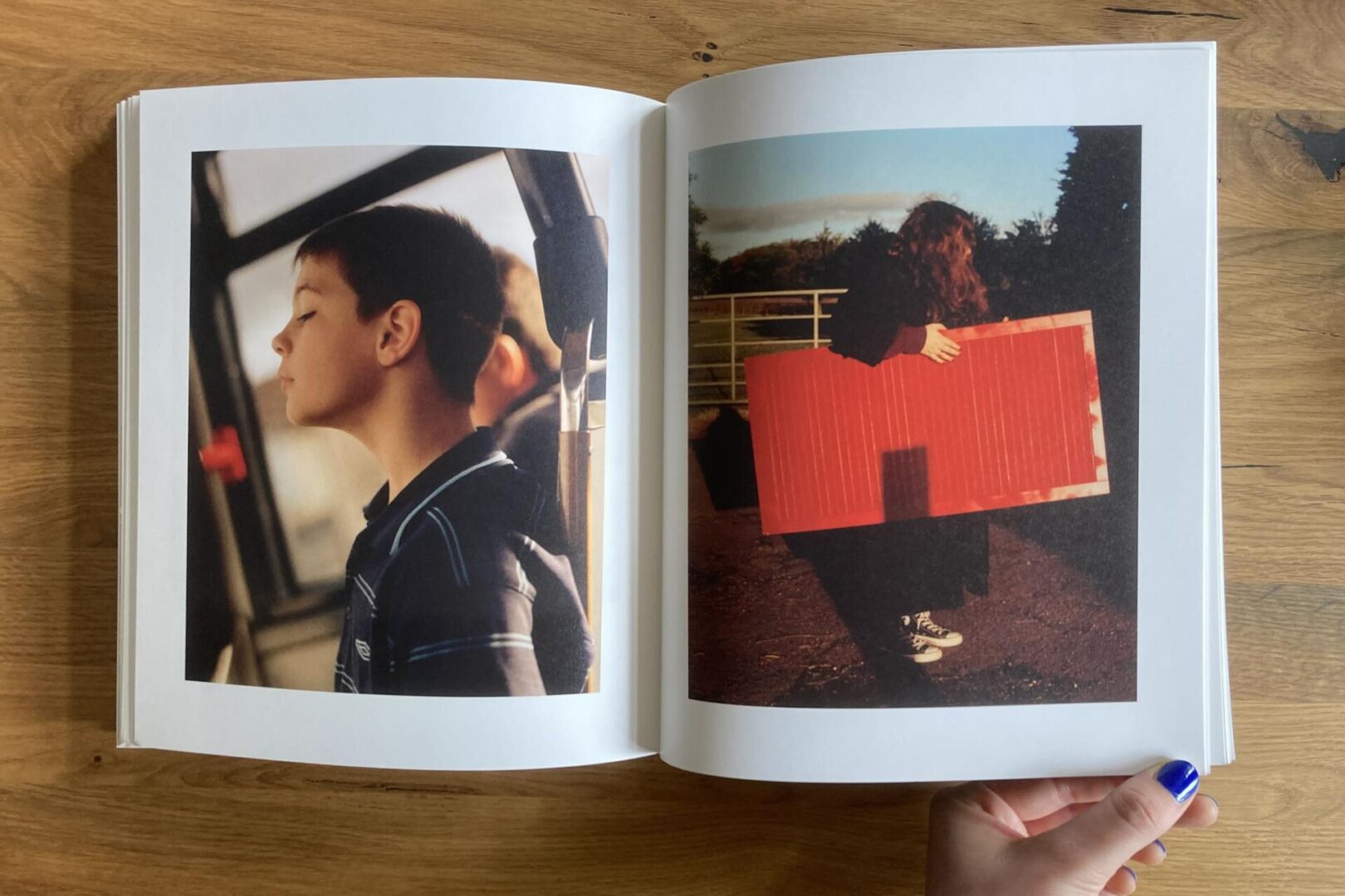 A book open to two photos: on the left, a boy with closed eyes sits by a window; on the right, a person outdoors holds a large red rectangular object, with their face mostly obscured by hair and shadows.