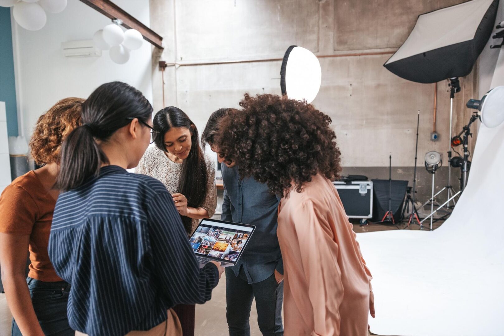 Five people stand in a photography studio, gathered around and looking at images on a tablet. Professional lighting equipment and a white backdrop are visible in the background.
