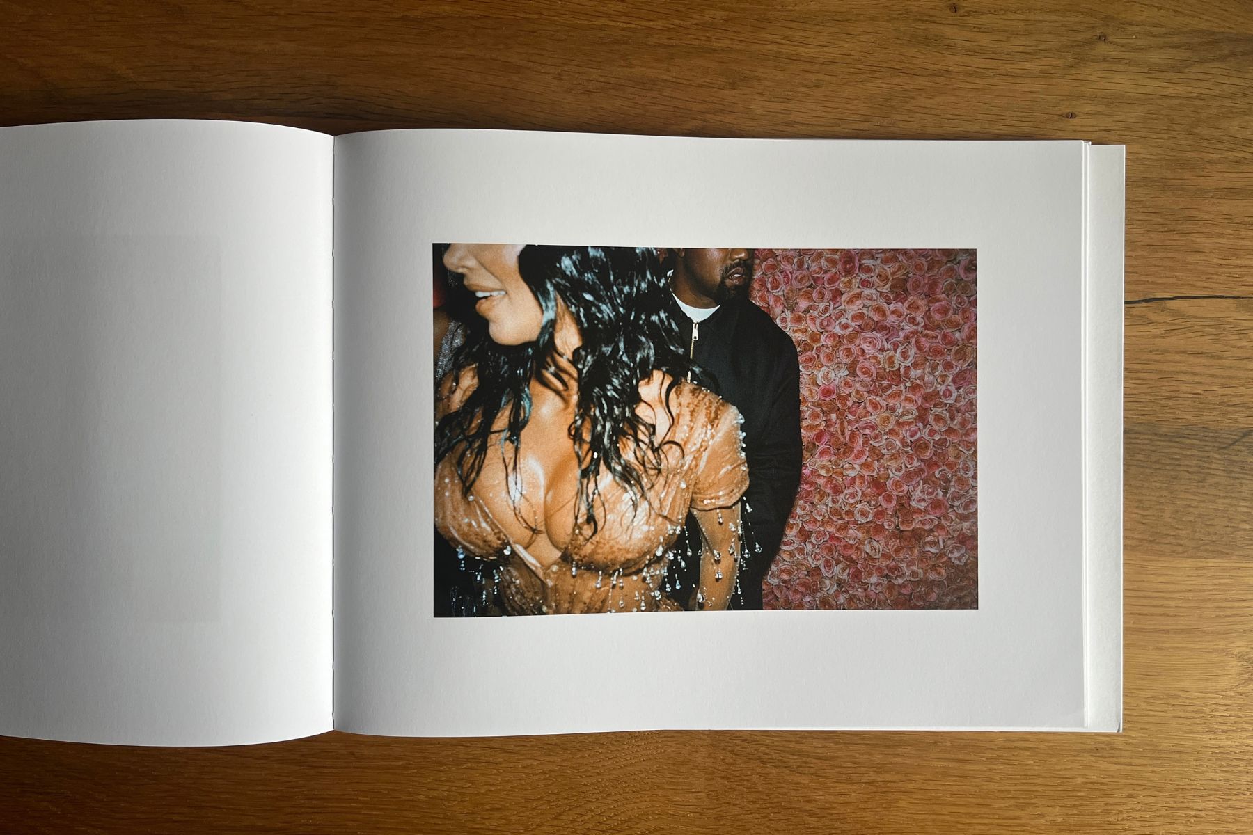 Open photobook showing a woman in a beaded top in front of a wall of pink roses, with a man standing behind her.