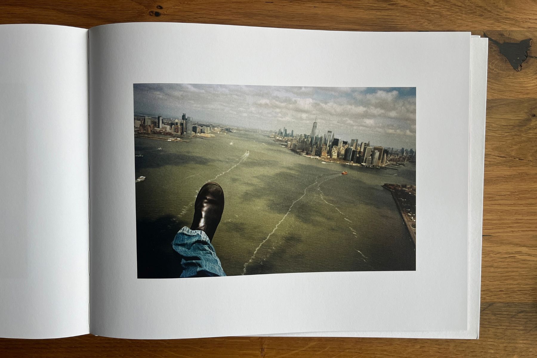 Open photobook showing a boot extending above the water, with the Manhattan skyline in the distance.