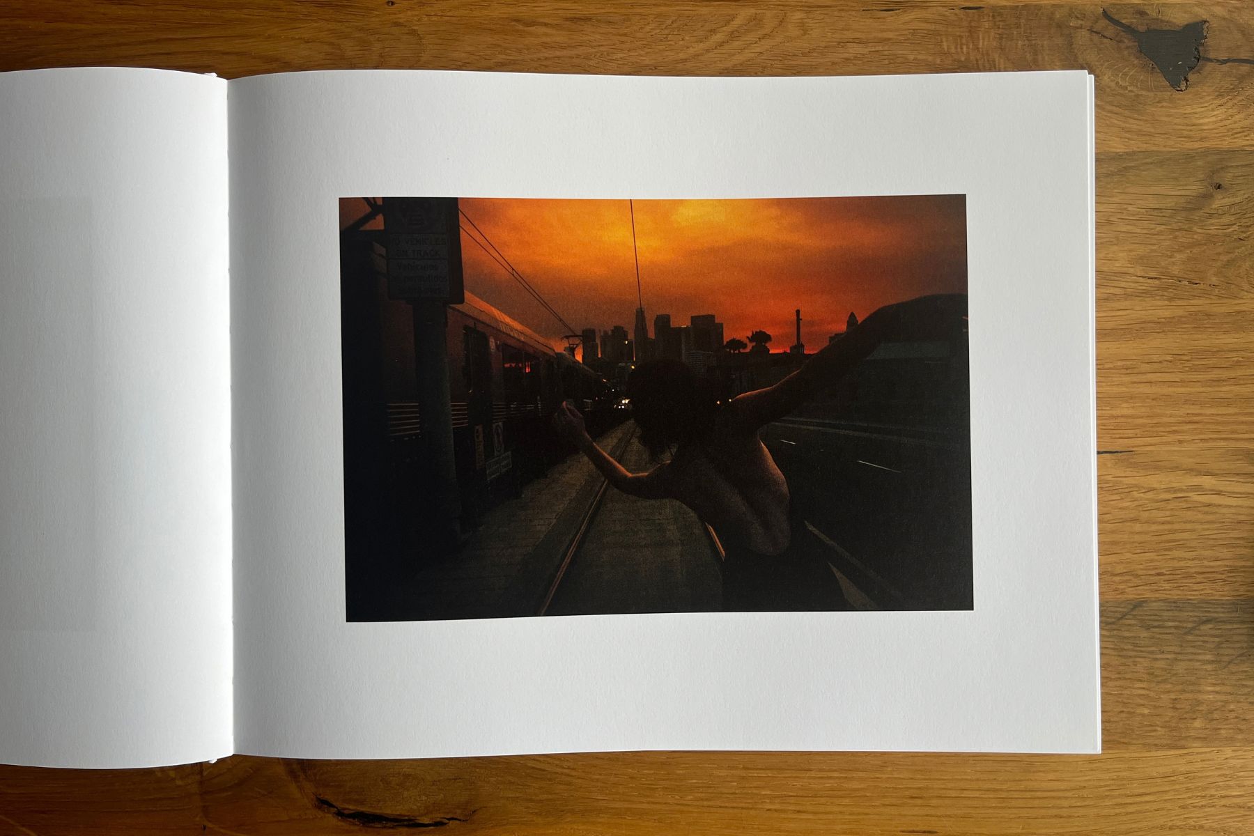 Open photobook showing a silhouetted figure next to a train in the sunset, with a city skyline in the distance.