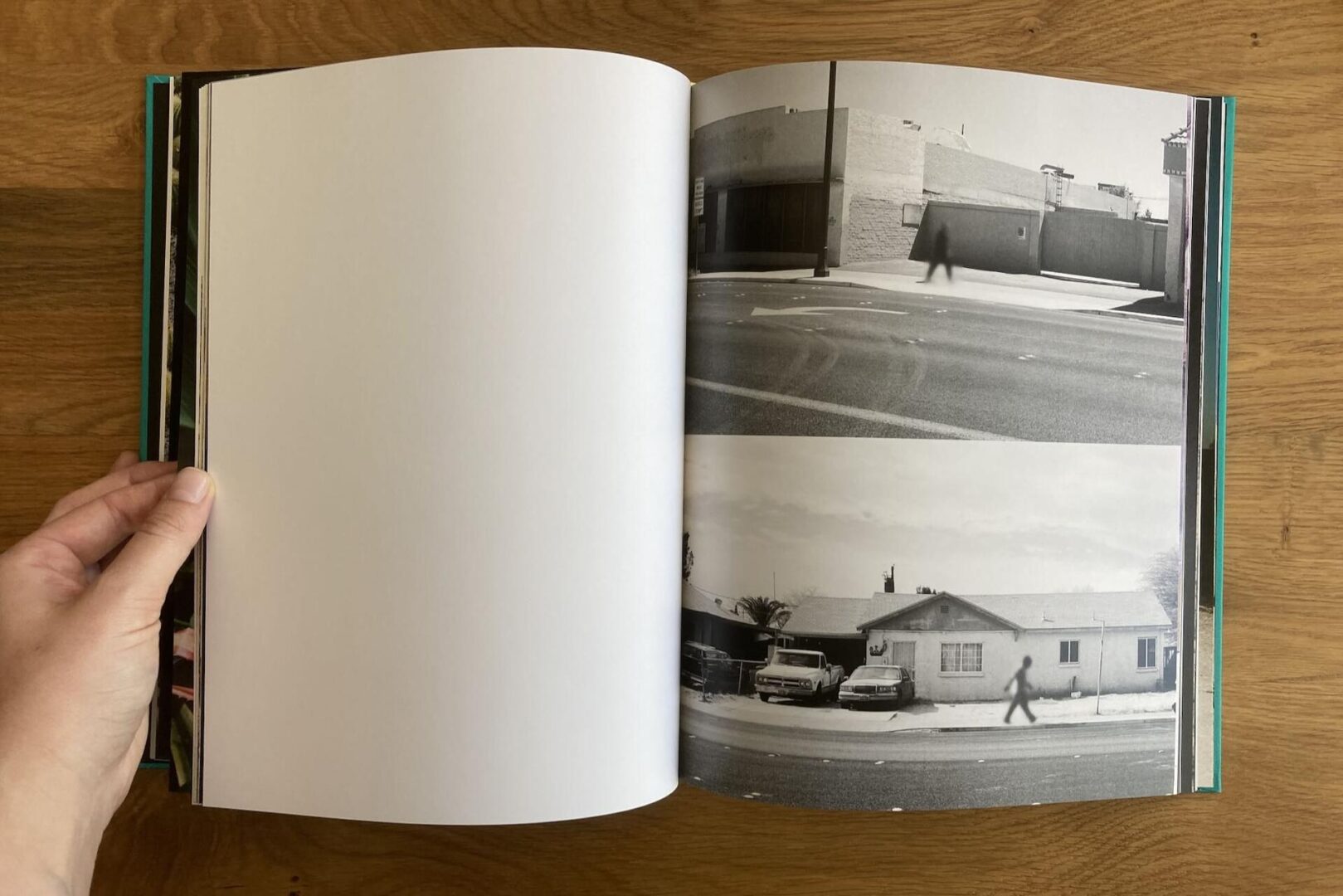 An open book on a wooden surface shows two black-and-white photos: the top is a shadowy figure walking past a building, the bottom is a person walking on a sidewalk in front of houses and parked cars.