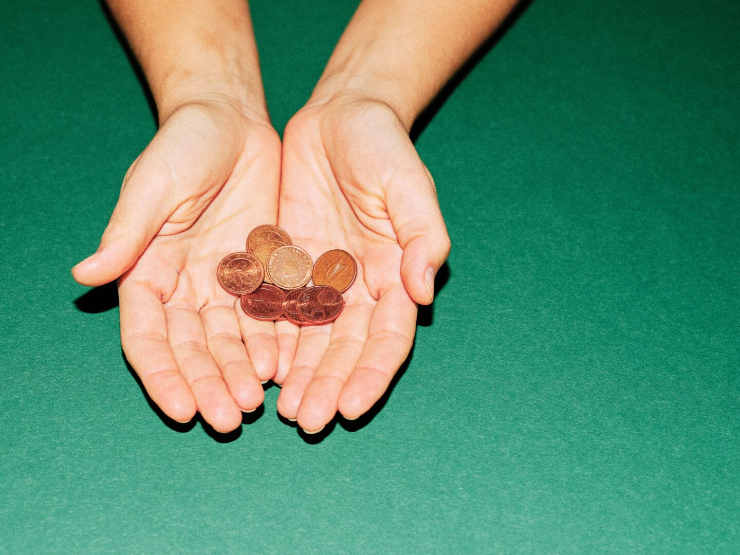 Two open hands holding a few copper coins against a green background.